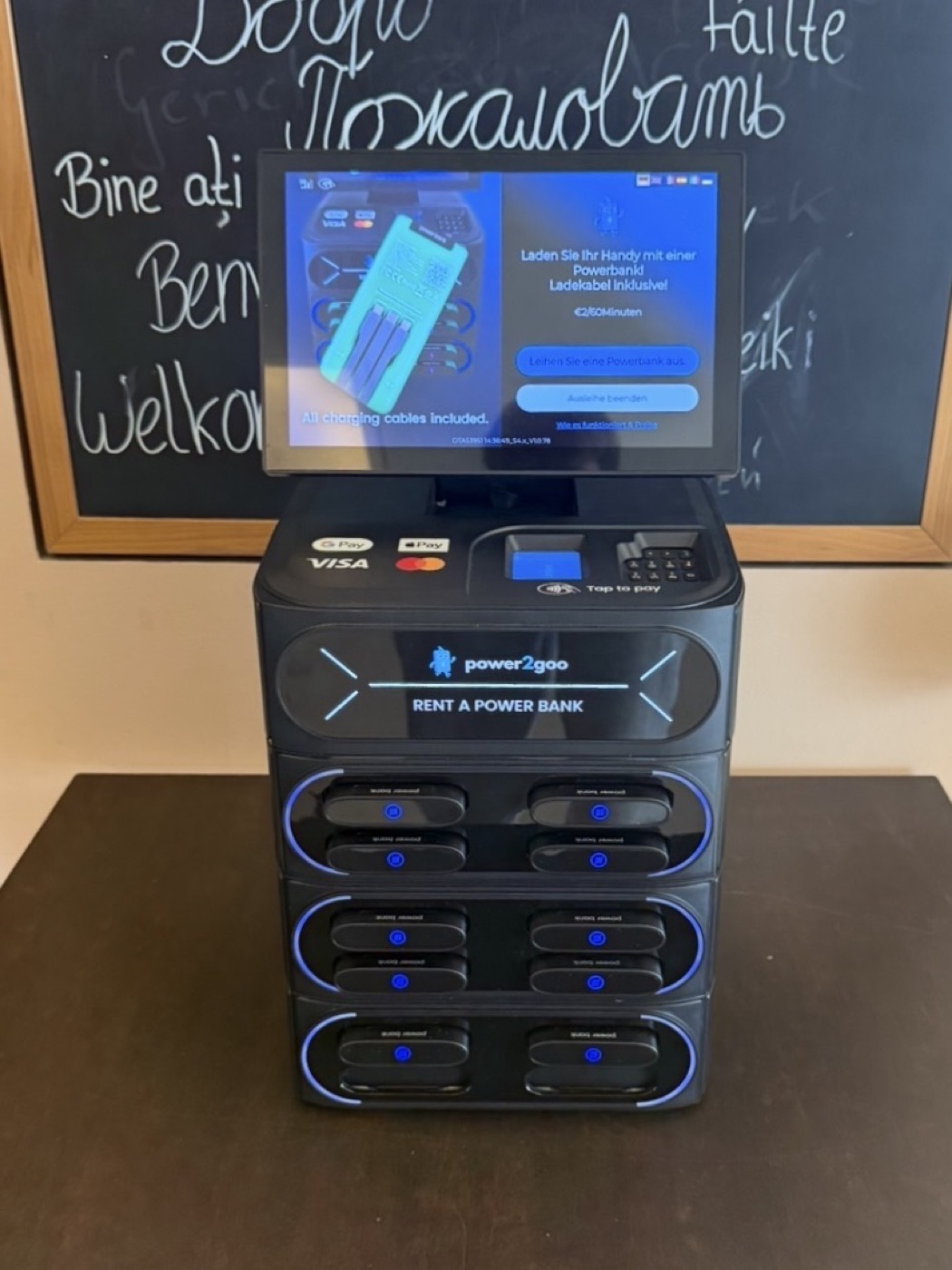 power2goo Powerbank-Station in einem Café in Nürnberg, dahinter eine Tafel mit Begrüßungen in vielen Sprachen
